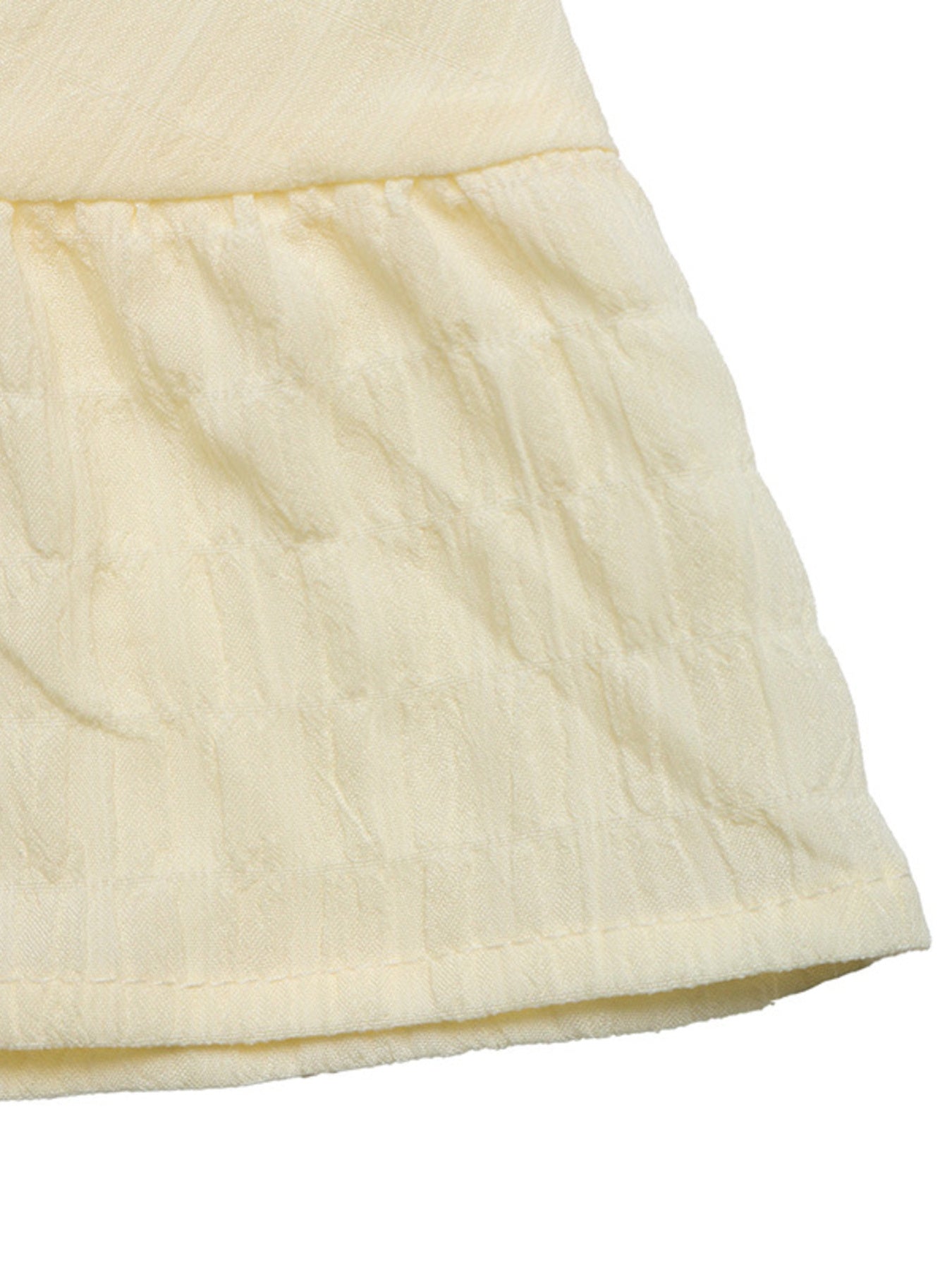 Smocked spaghetti strap dress fabric close-up in pale yellow with ruched tiers.